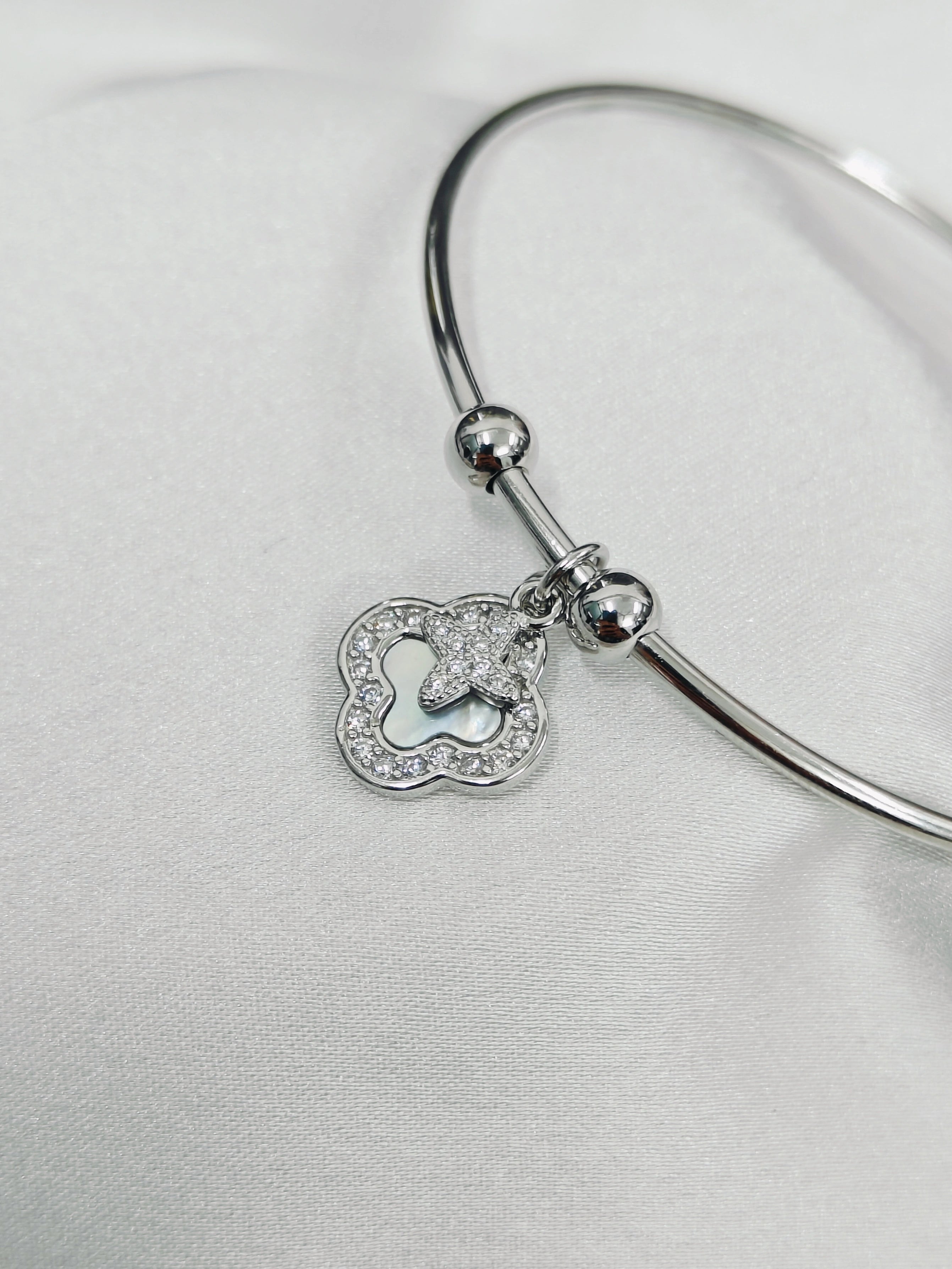 Silver bangle with a heart-shaped charm on a light gray background